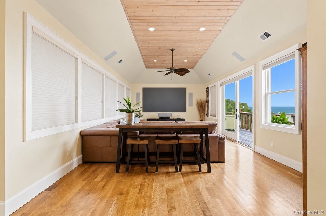 Dining and living area with a wood-plank ceiling, sliding doors, and an ocean view.
