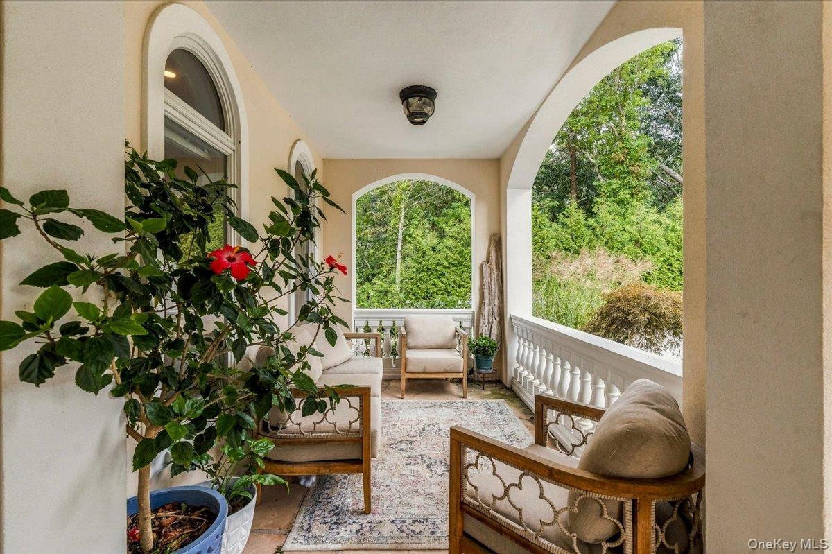 Covered porch with arched openings, cushioned seating, and potted plants overlooking greenery.