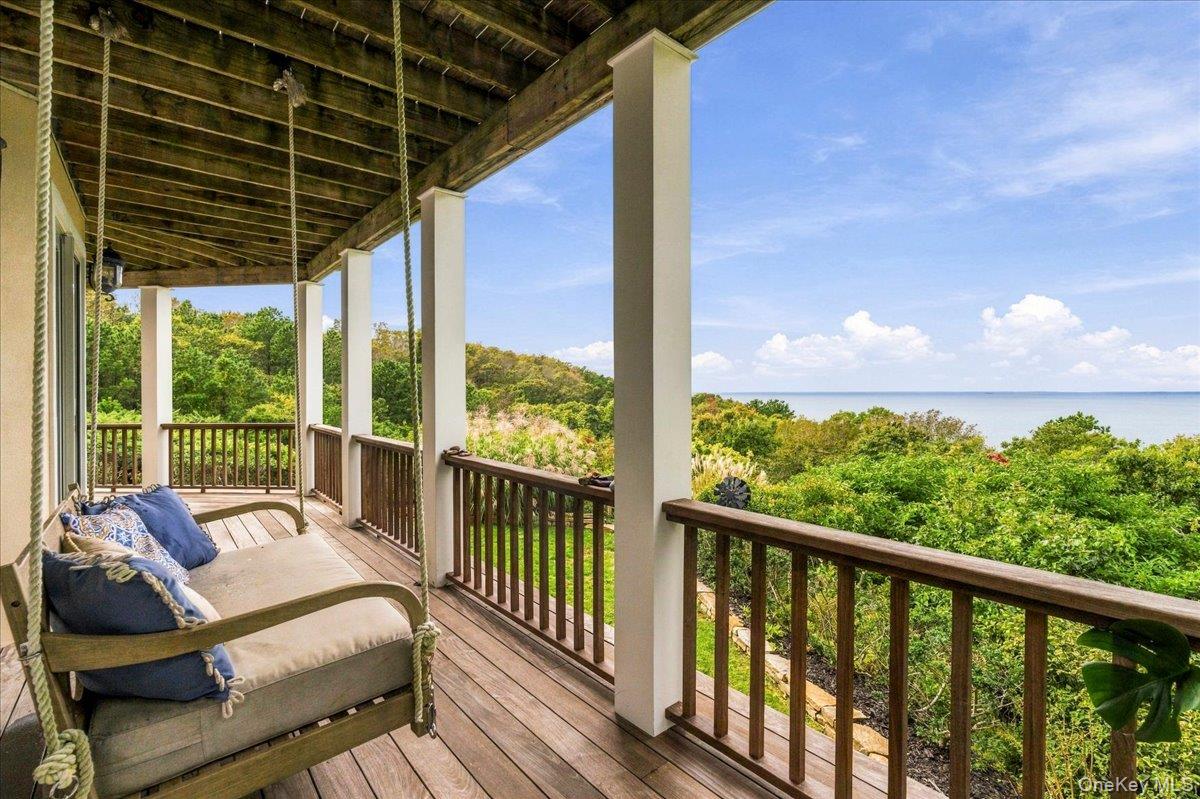 Covered porch with a cushioned hanging swing overlooking greenery and water.