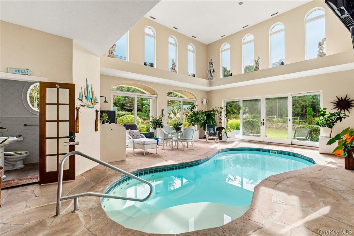 Indoor pool beneath tall arched windows, with stone decking and glass doors to the garden.