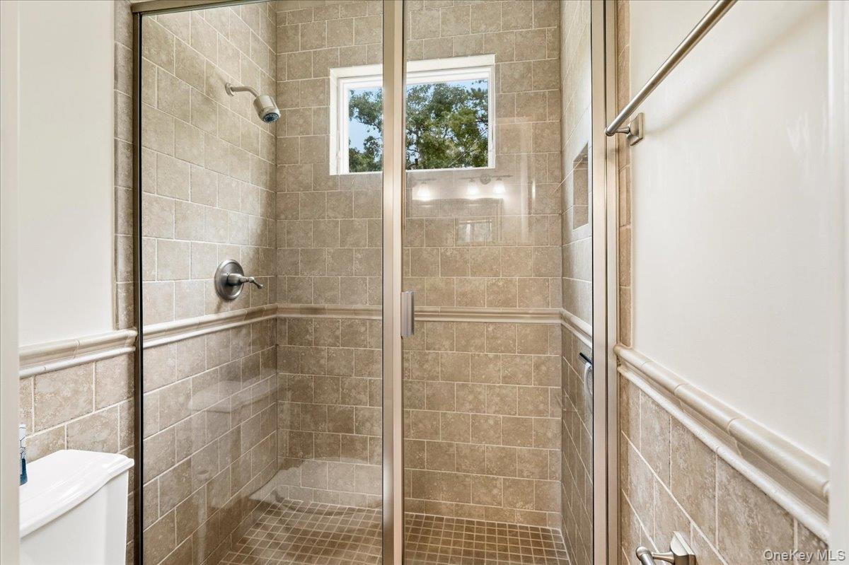 Tiled walk-in shower with a glass enclosure, chrome fixtures, and a small window.