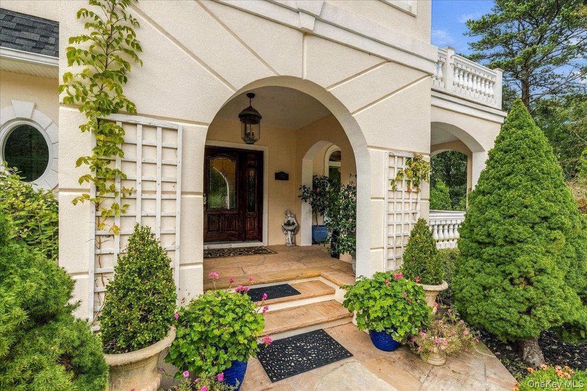 Cream-colored home entrance with an arched porch, dark wood door, stone steps, and flowering pots.