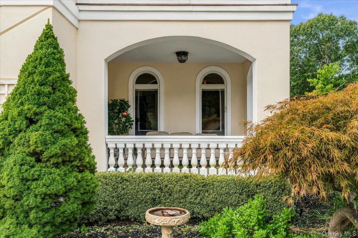 Covered front porch with arched entry, tall windows, white balustrade, and landscaped shrubs.
