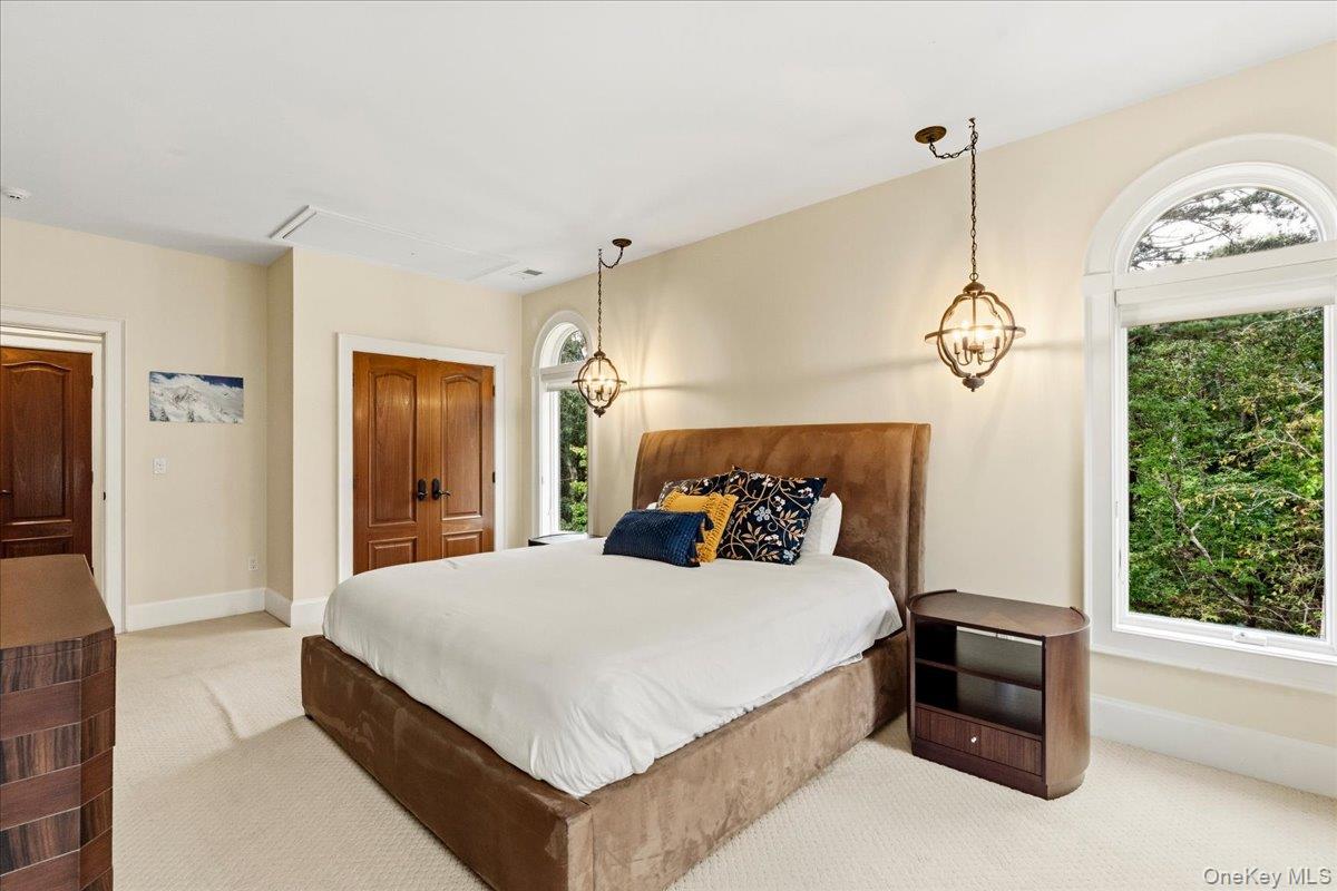 Bedroom with a large upholstered bed, arched windows, and dark wood doors.