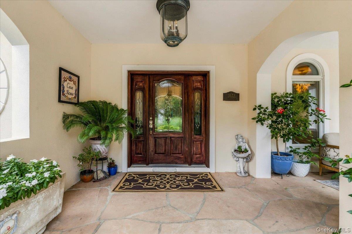 Covered front entry with a carved wooden door, arched window, potted plants, and tiled porch.