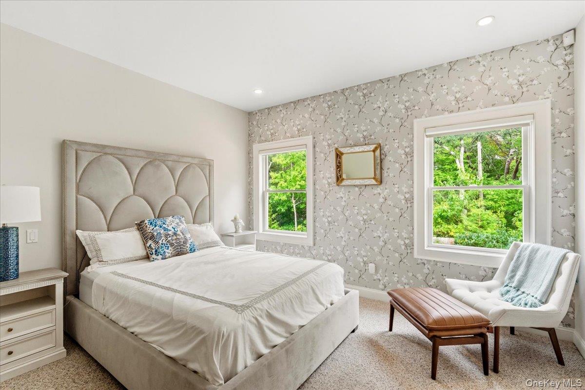 Staged bedroom with a white bed, floral wallpaper, and windows overlooking greenery.