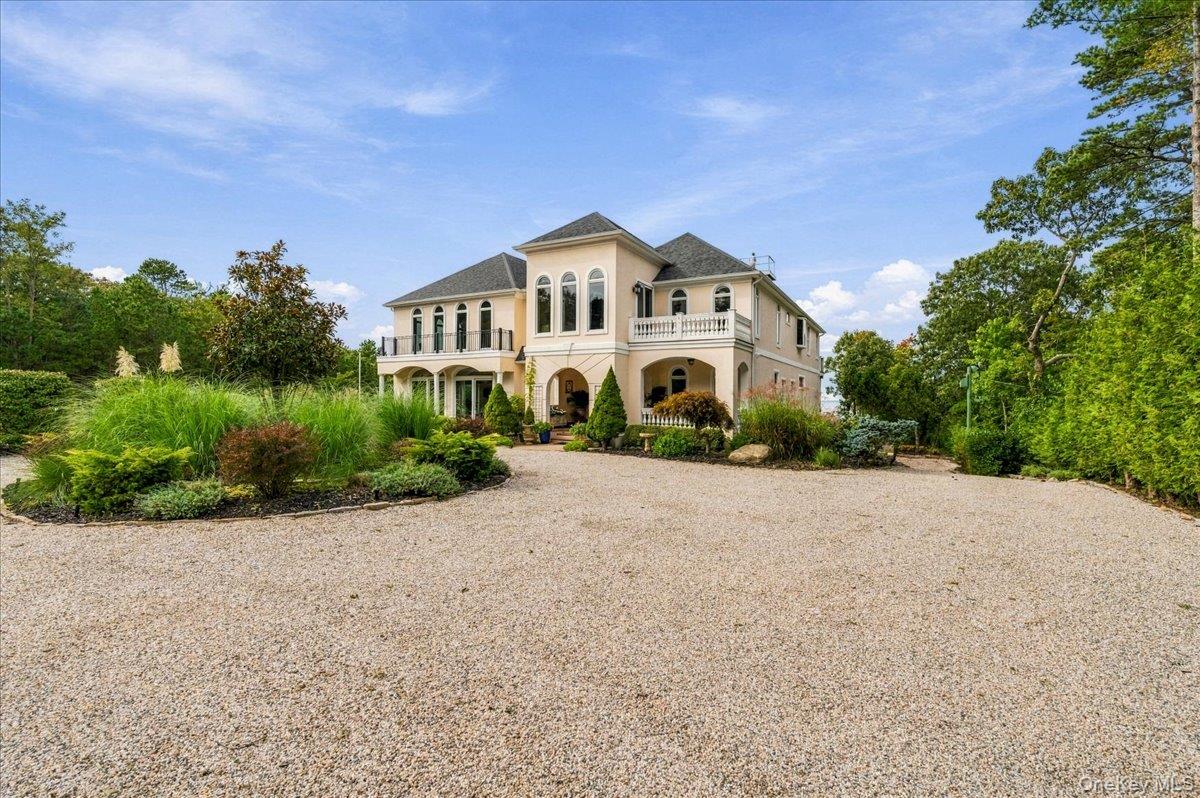Large cream house with arched openings and balconies beyond a broad gravel driveway.
