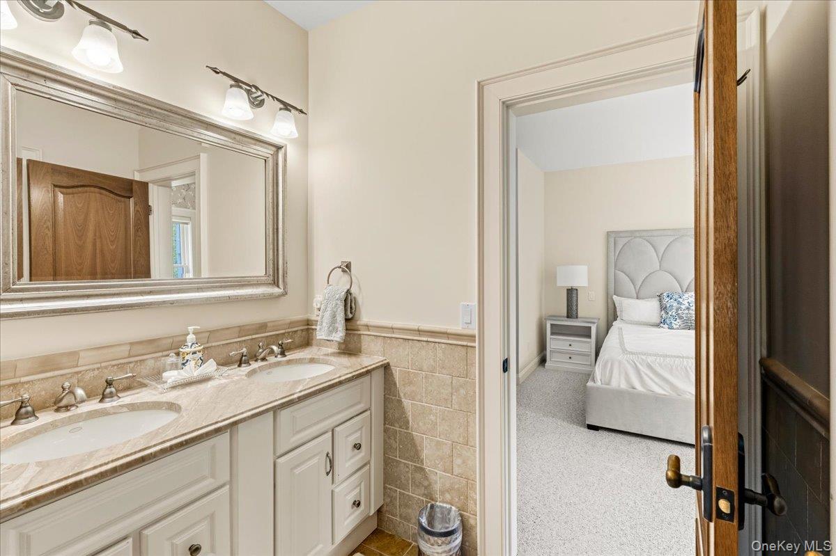 Bathroom with a double-sink vanity and stone countertop, opening onto a bedroom.