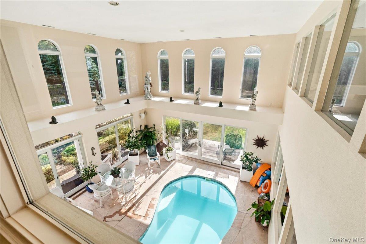 Indoor swimming pool beneath tall arched windows, with a small seating area and patio doors.