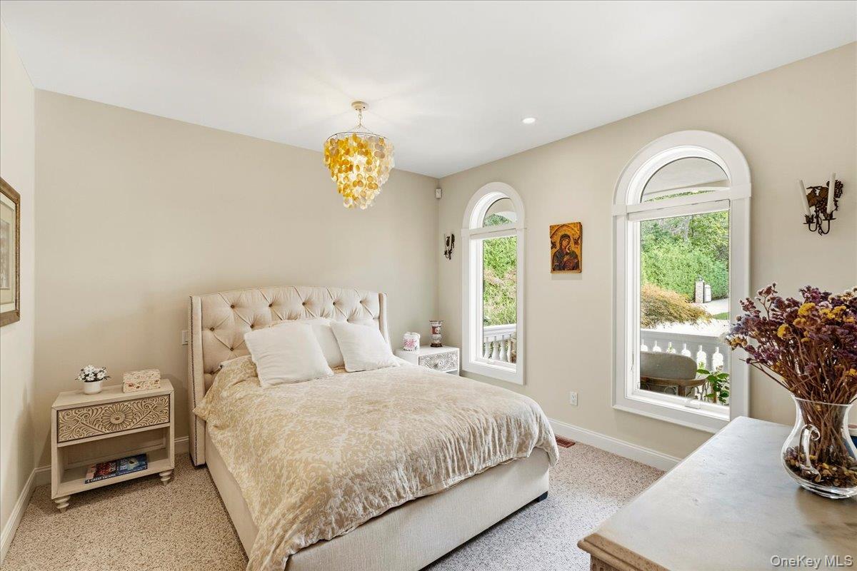 Bedroom with a tufted bed, gold-toned chandelier, and tall arched windows overlooking greenery.