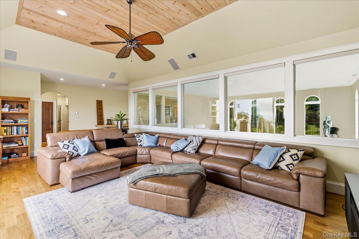 Living room with a tan leather sectional, vaulted wood ceiling, and windows overlooking water.