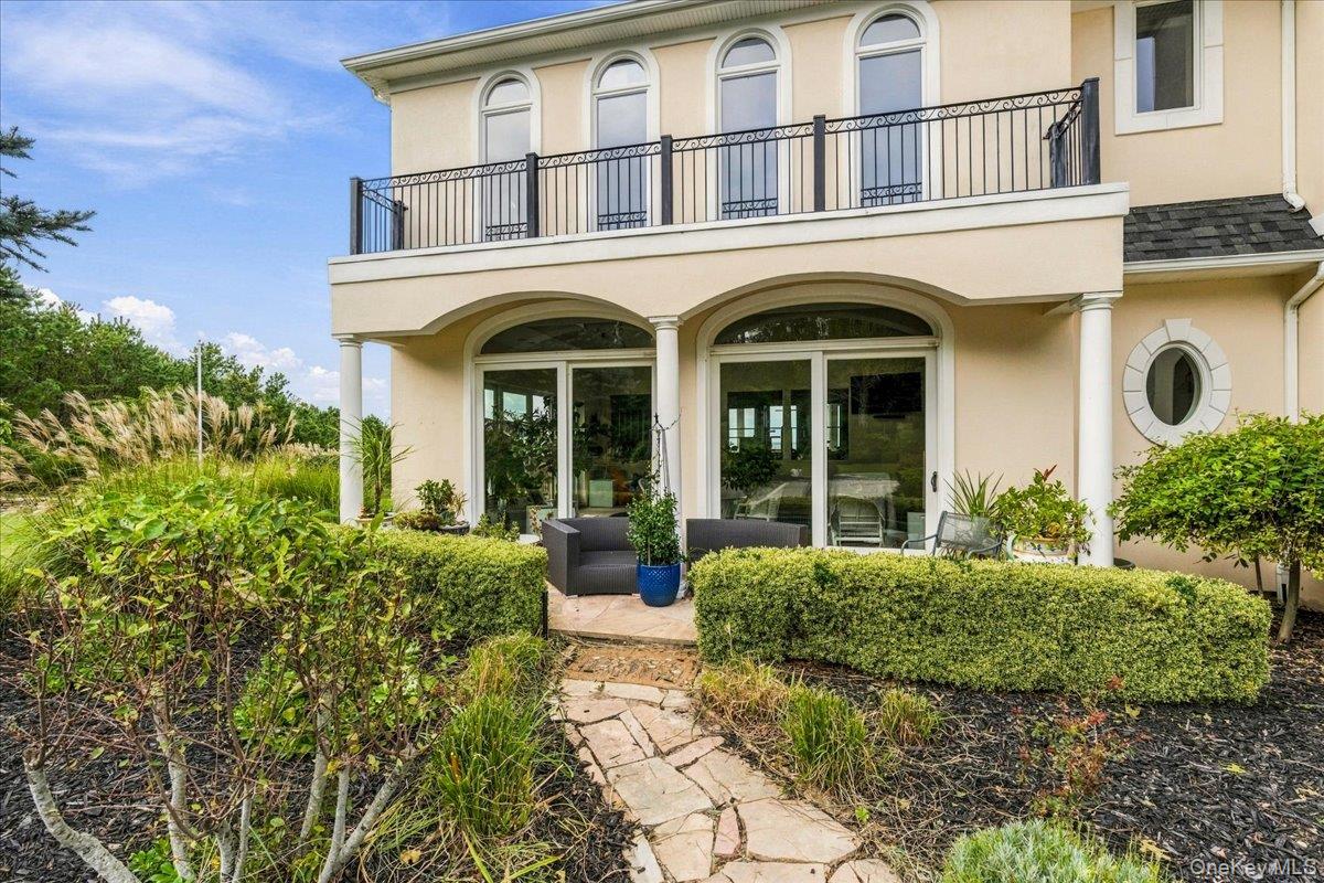 Cream-colored home with an arched-window balcony, furnished patio, hedges, and a stone path.