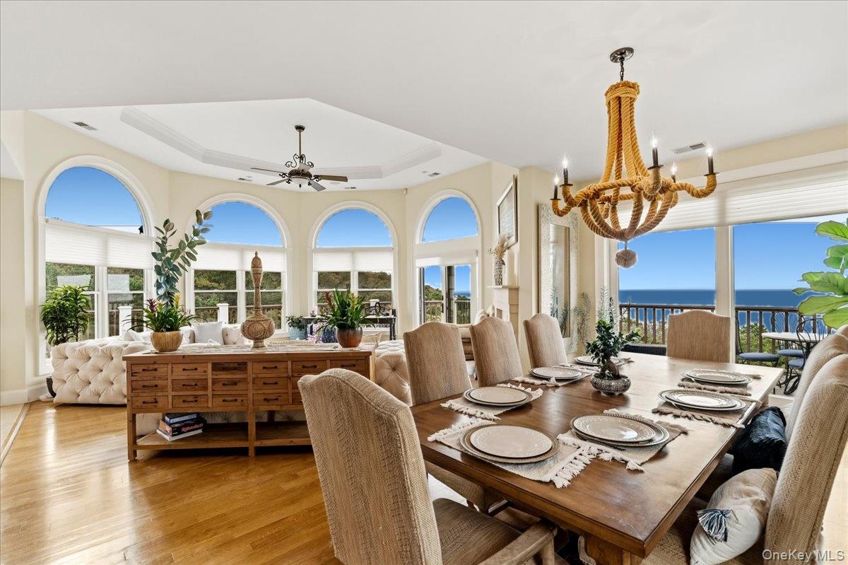 Dining area with arched windows overlooking the ocean and a large set table beneath a rope chandelier.
