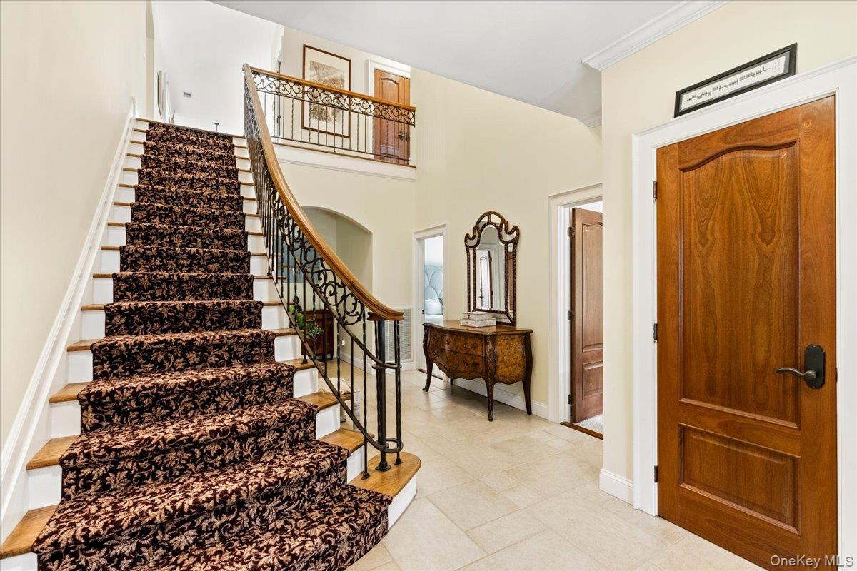 Entry foyer with a curved, patterned-carpet staircase and ornate iron railing beside a wooden front door.