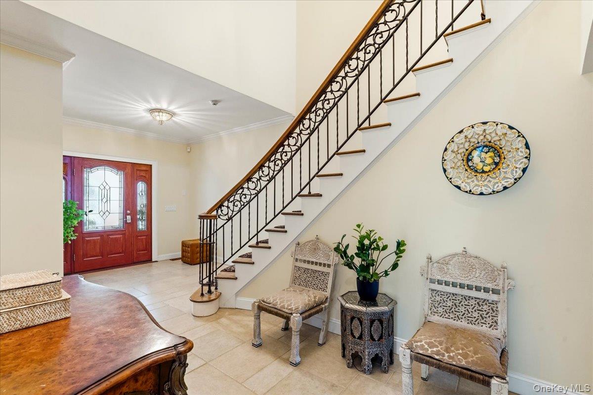 Entry foyer with tiled floor, decorative glass front door, and staircase with ornate iron railing.