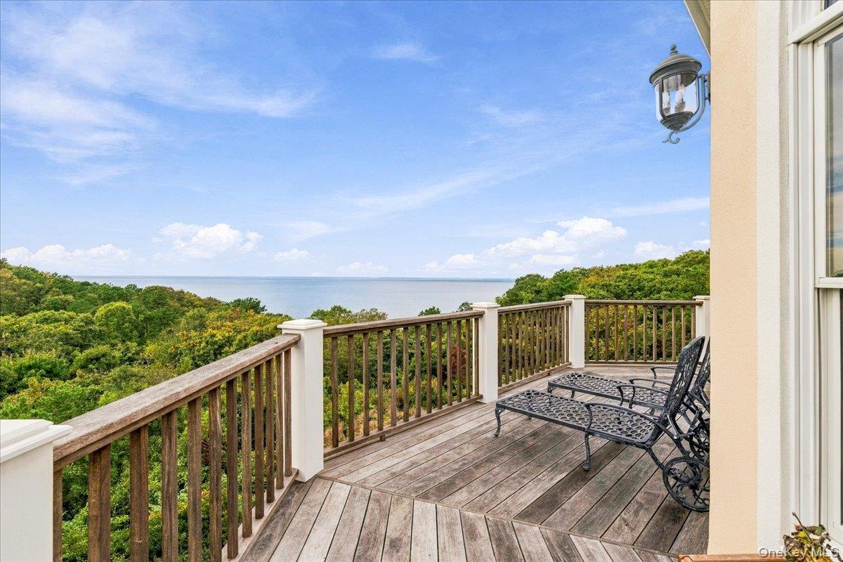 Wooden balcony with metal chairs overlooks treetops and water.