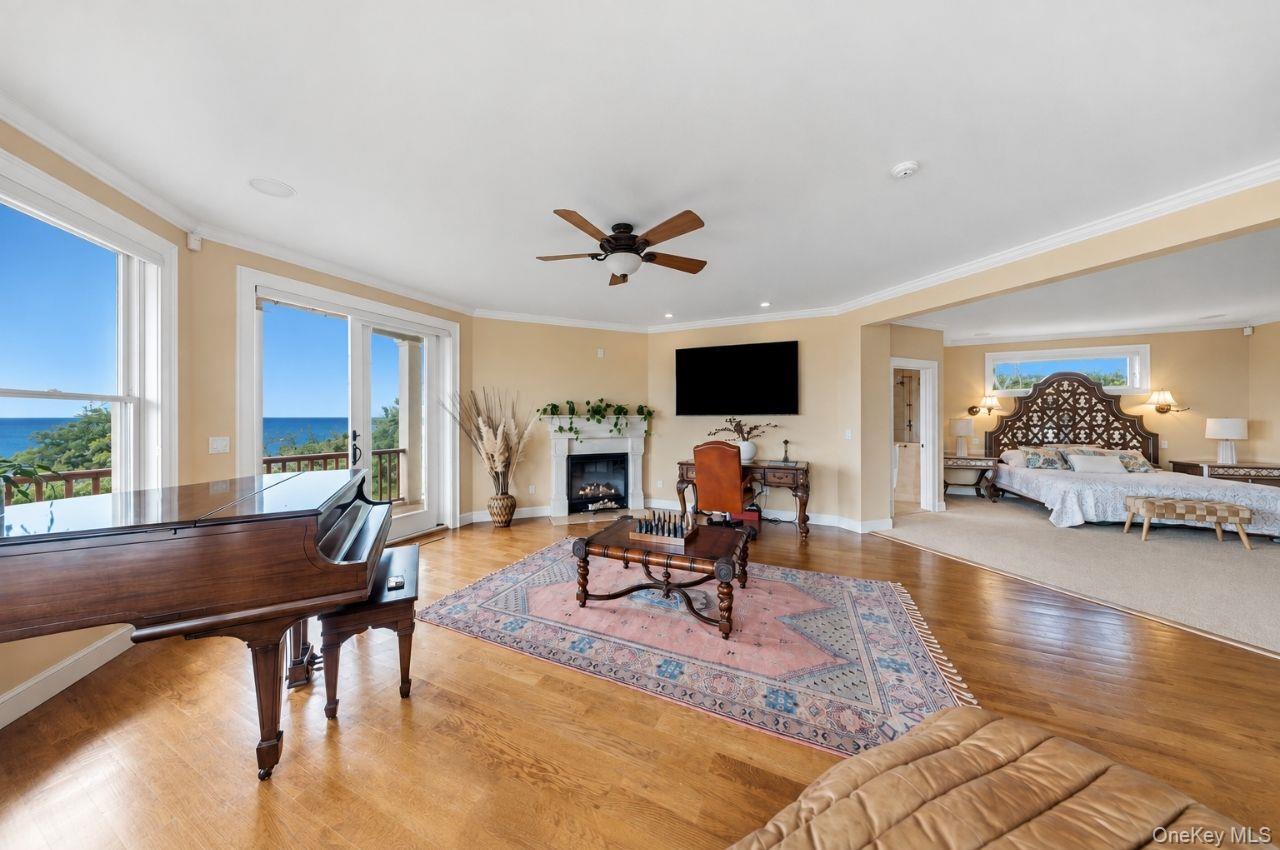 Living room with a grand piano and fireplace, opening to ocean views and an adjoining bedroom.