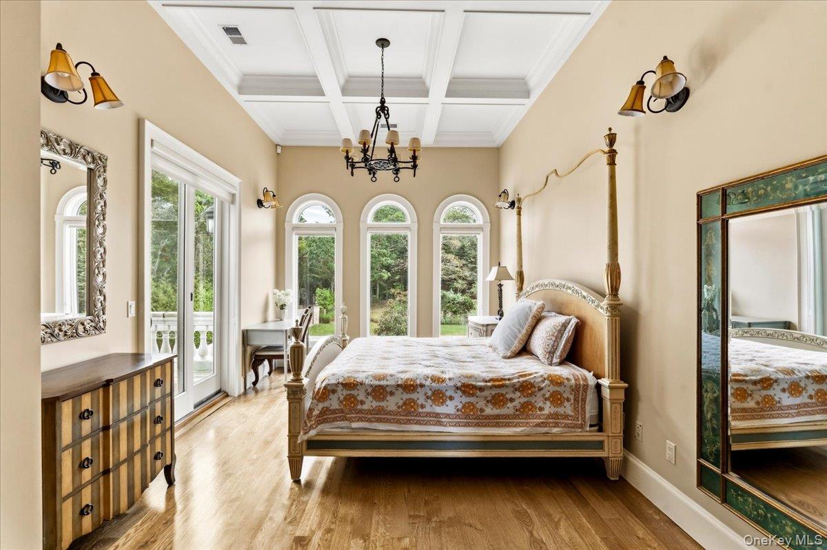Bedroom with an ornate four-poster bed, coffered ceiling, and arched windows overlooking greenery.