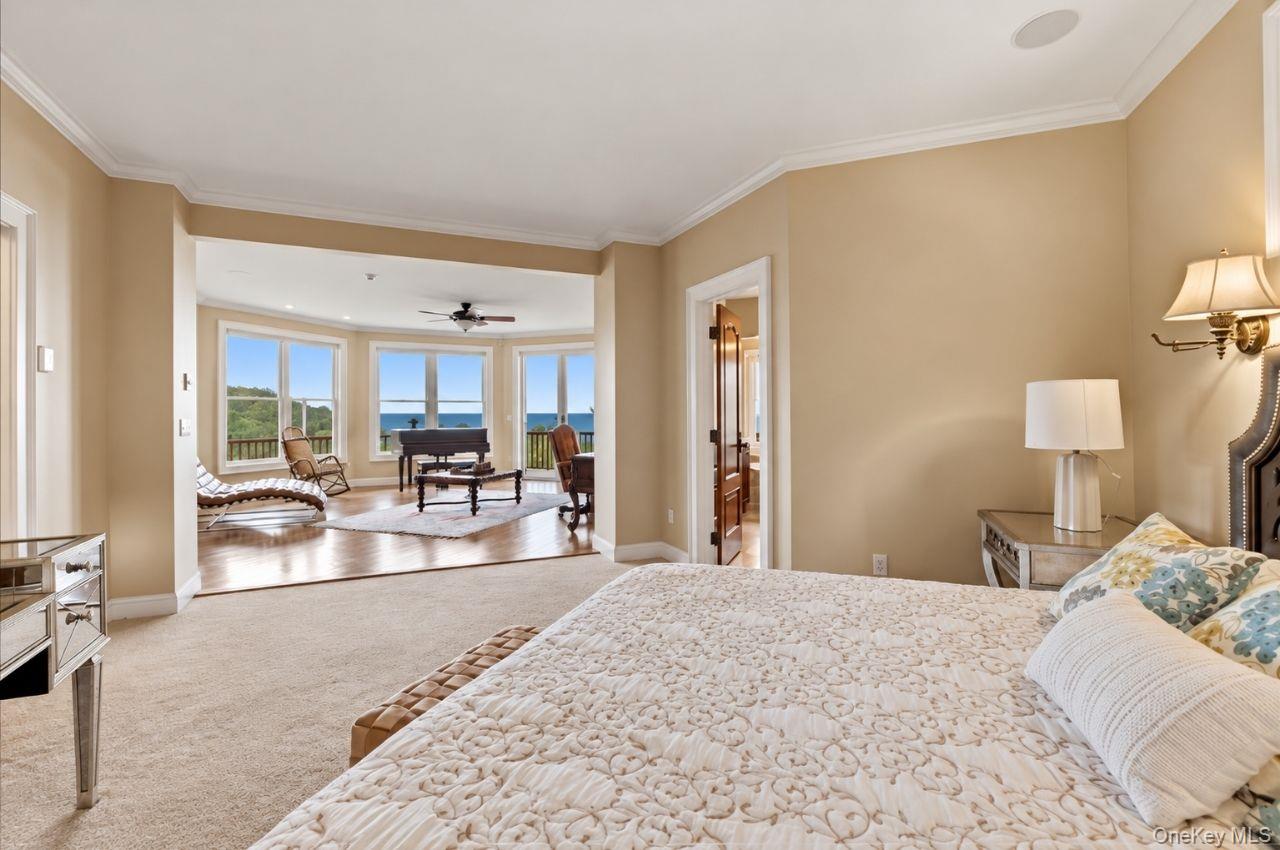 Furnished bedroom opening onto a sitting area with wide windows overlooking the water.