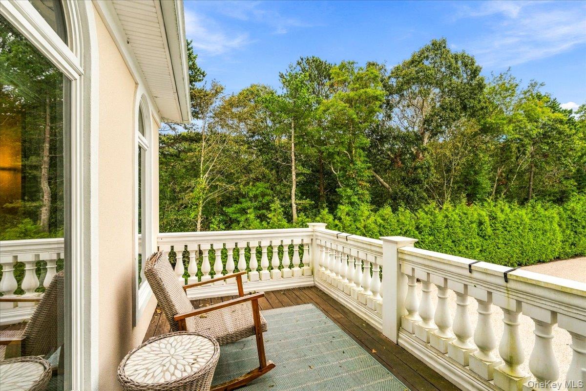 Wooden deck with white railings and wicker seating overlooking dense trees.