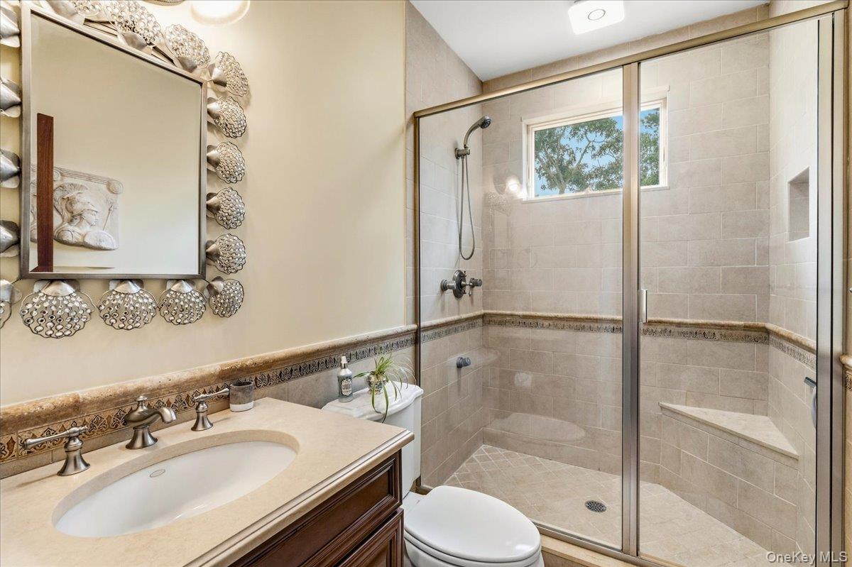 Bathroom with glass-enclosed tiled shower, built-in bench, and ornate mirror above the vanity.