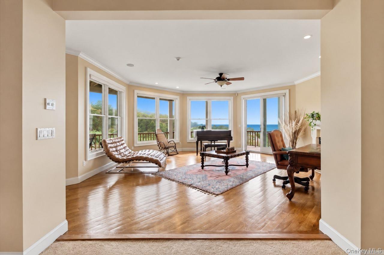 Living room with hardwood floors, leather seating, a grand piano, and large windows overlooking the water.