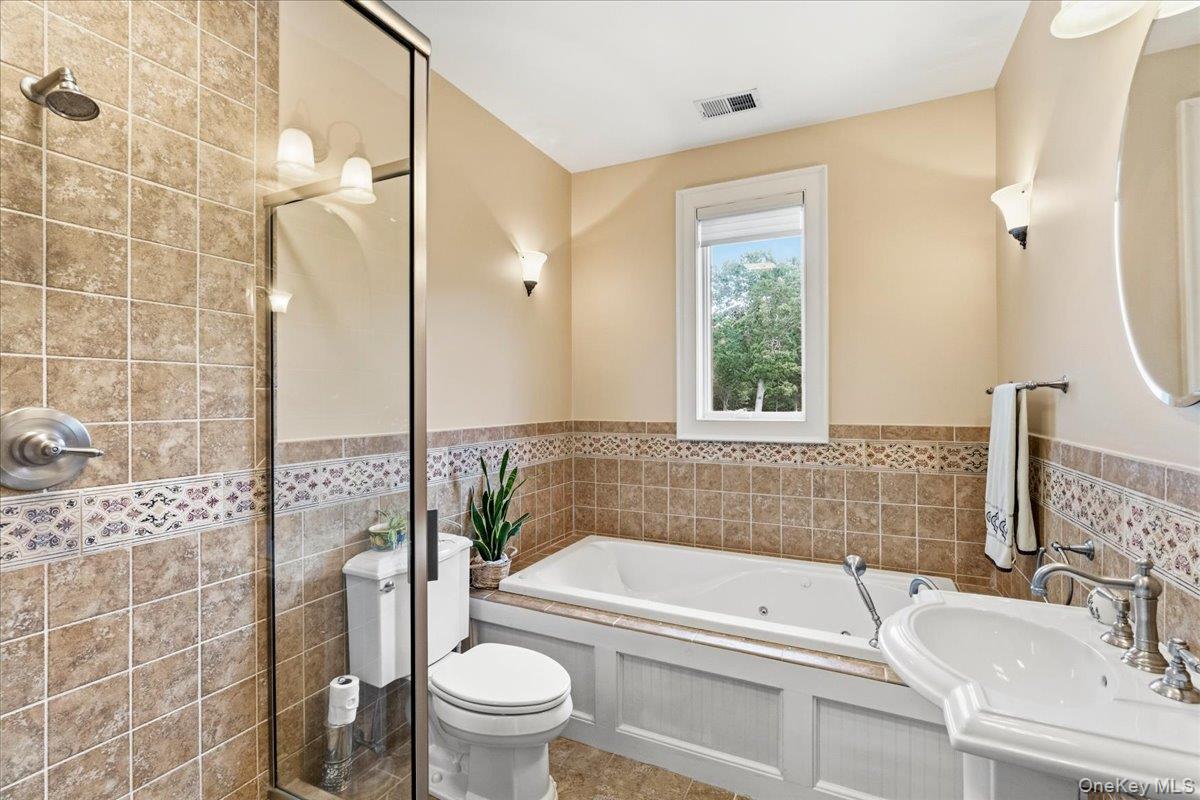 Tiled bathroom with a glass shower, built-in soaking tub, and window overlooking trees.