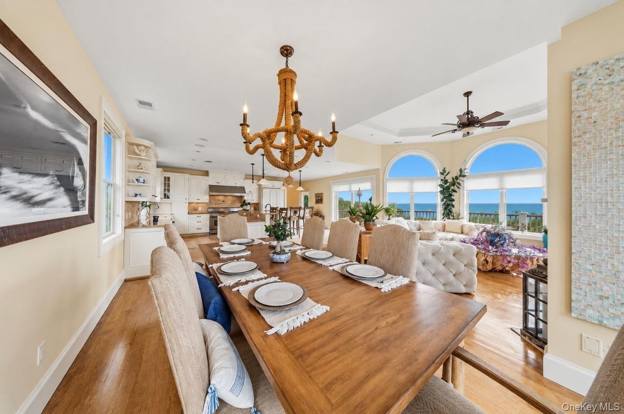 Dining area with a set wooden table, open kitchen, and ocean views through arched windows.