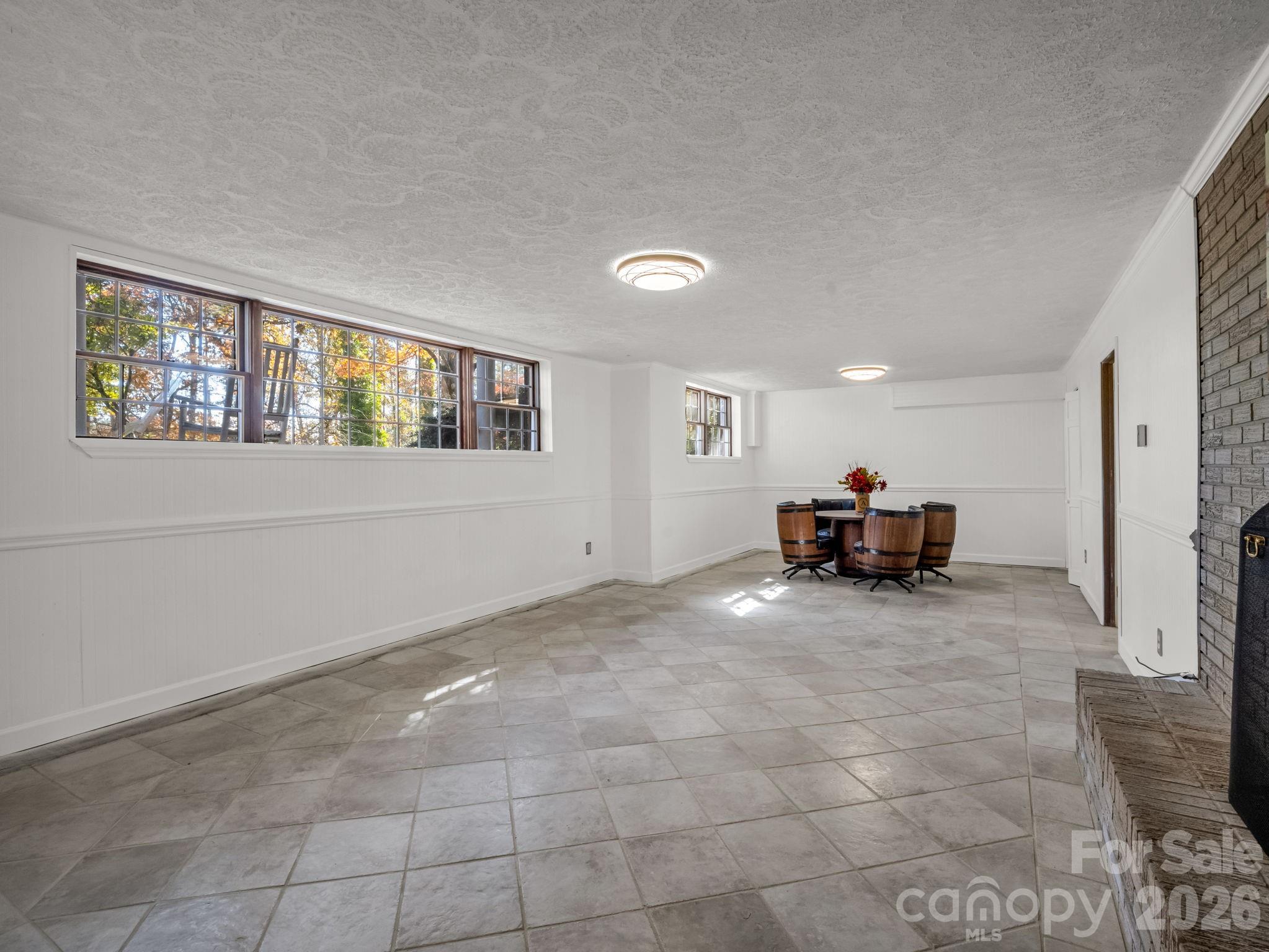 Dining room with large windows, tiled floors, and a round table with barrel-style chairs.