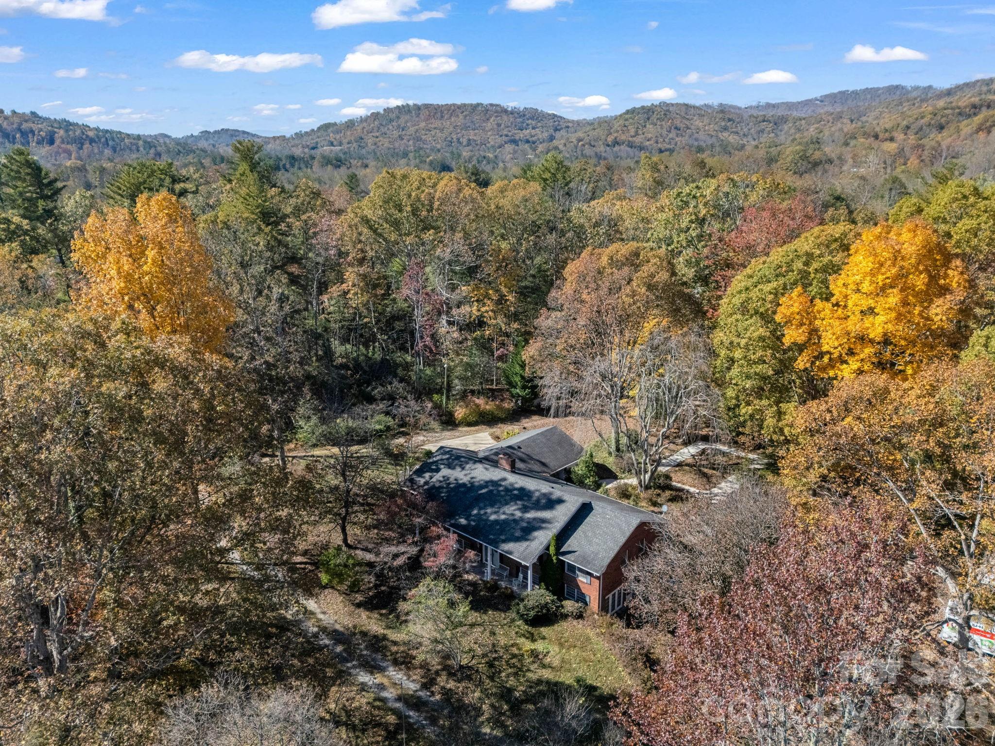 Aerial view of a brick home surrounded by autumn trees, with wooded mountain ridges beyond.