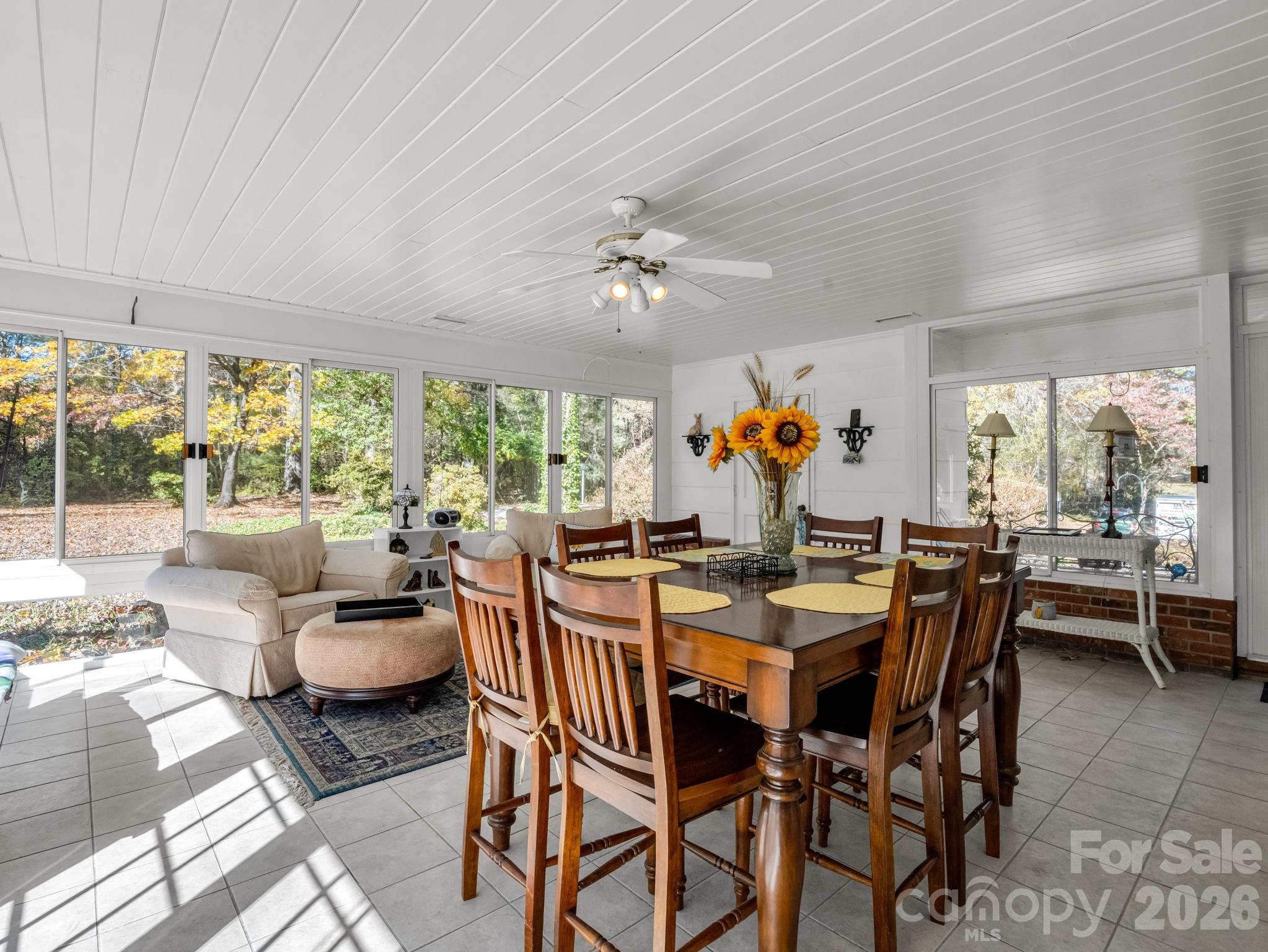 Dining area with a large wooden table and wide windows overlooking autumn trees.