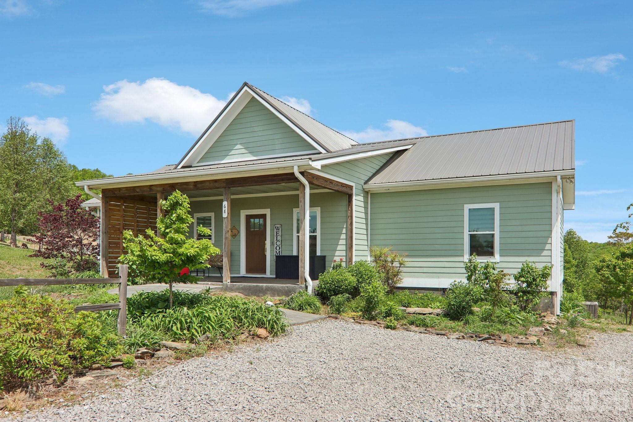 Green-sided home with a covered timber porch, metal roof, and gravel driveway.