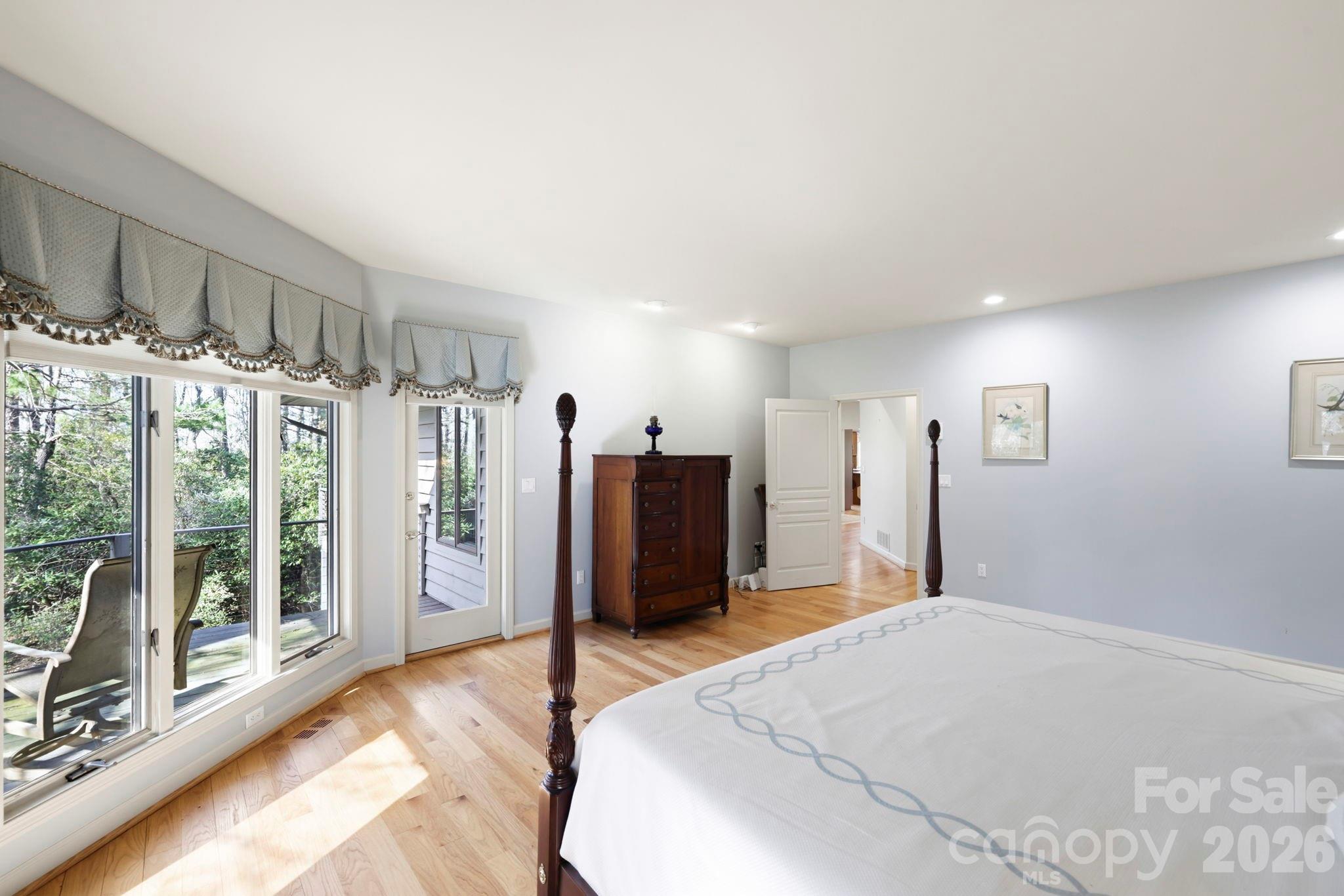 Bedroom with a four-poster bed, hardwood floors, and large windows overlooking trees.