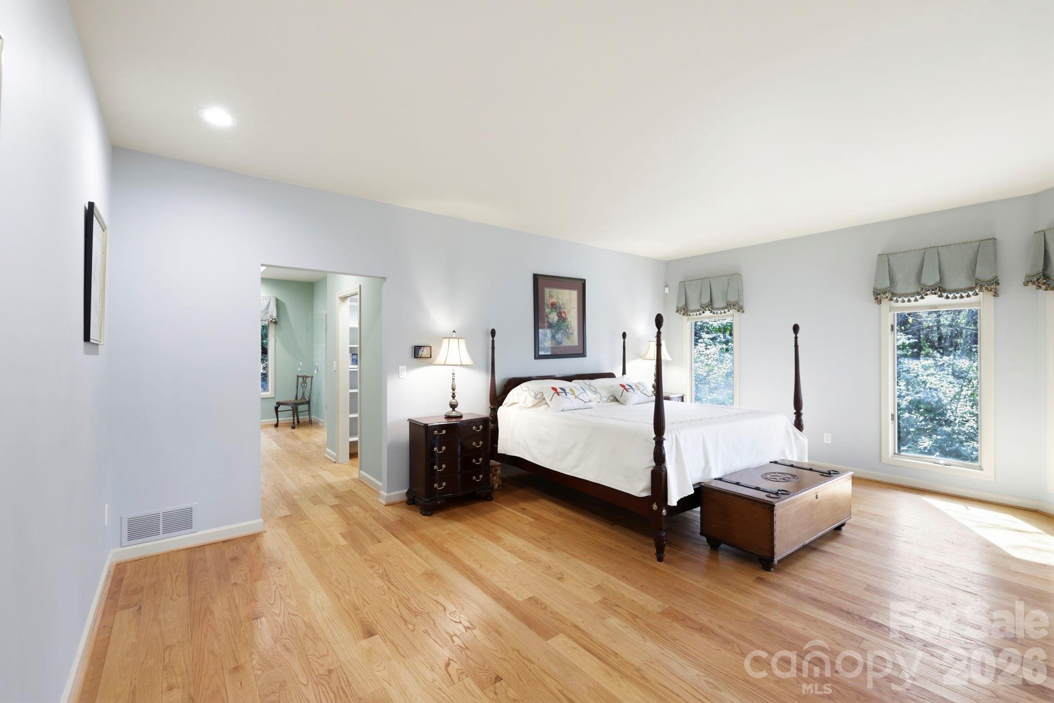 Furnished bedroom with a four-poster bed, hardwood floors, and large windows overlooking trees.