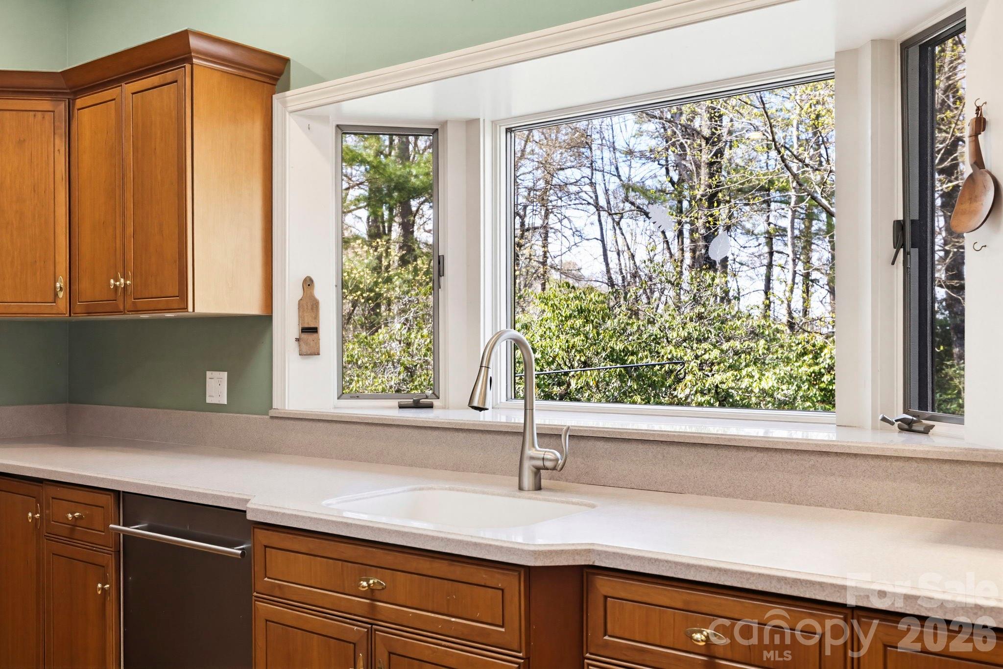 Kitchen with warm wood cabinets, a white sink, and large windows overlooking trees.