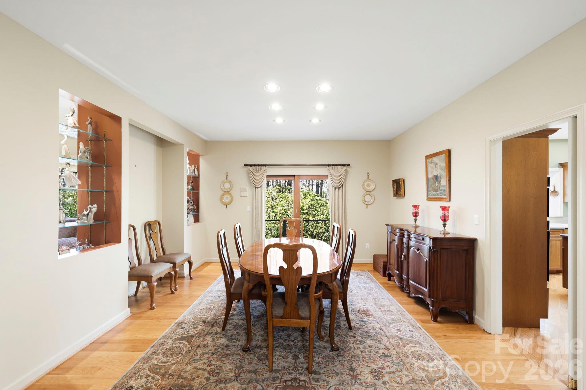Dining room with an oval wooden table, carved chairs, built-in display niches, and a dark wood sideboard.