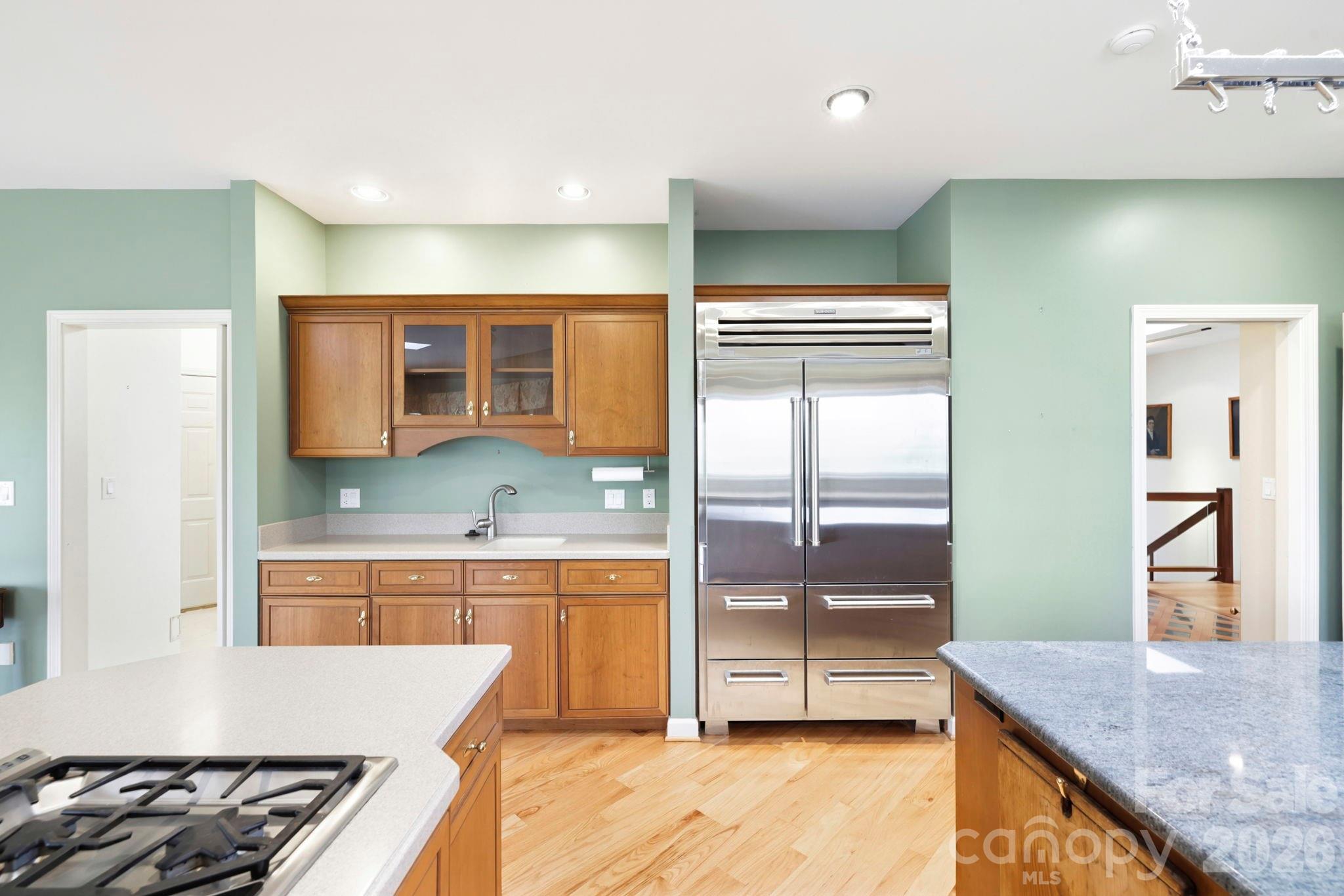 Kitchen with wood cabinets, a stainless steel refrigerator, and two stone-topped islands.