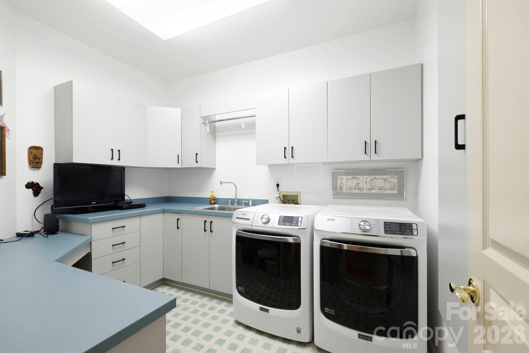 Laundry room with white cabinetry, blue counters, a utility sink, and Maytag washer and dryer.