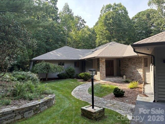 Single-story stone-and-siding home with a curved stone walkway and mature trees.