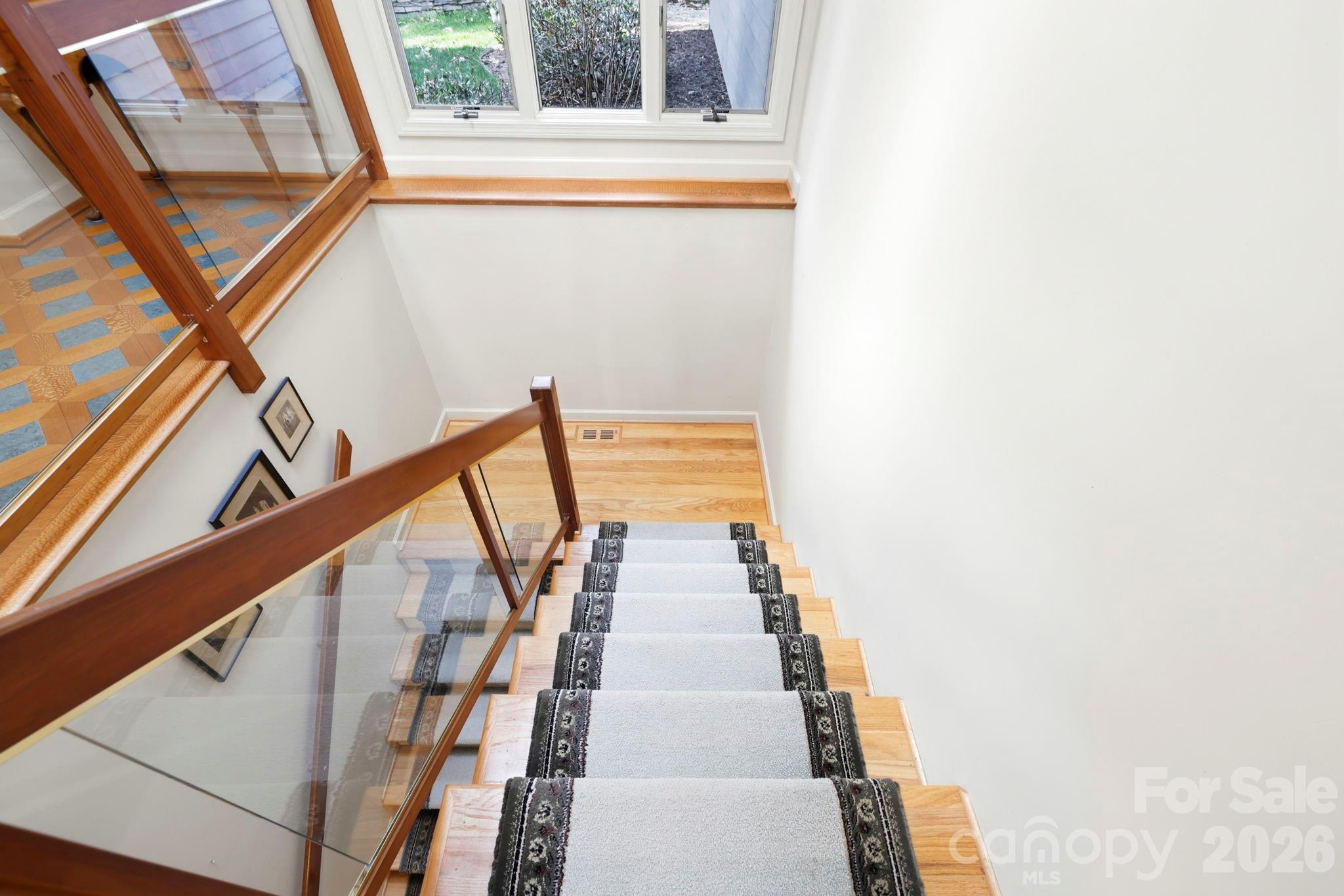 Wooden staircase with a gray runner and wood-and-glass railing beneath a window.