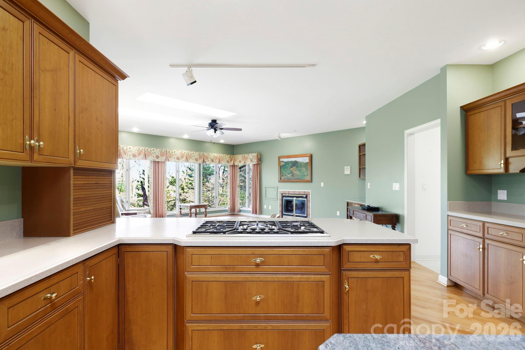 Kitchen with warm wood cabinetry, a large gas-cooktop island, and views into a living area with a fireplace.