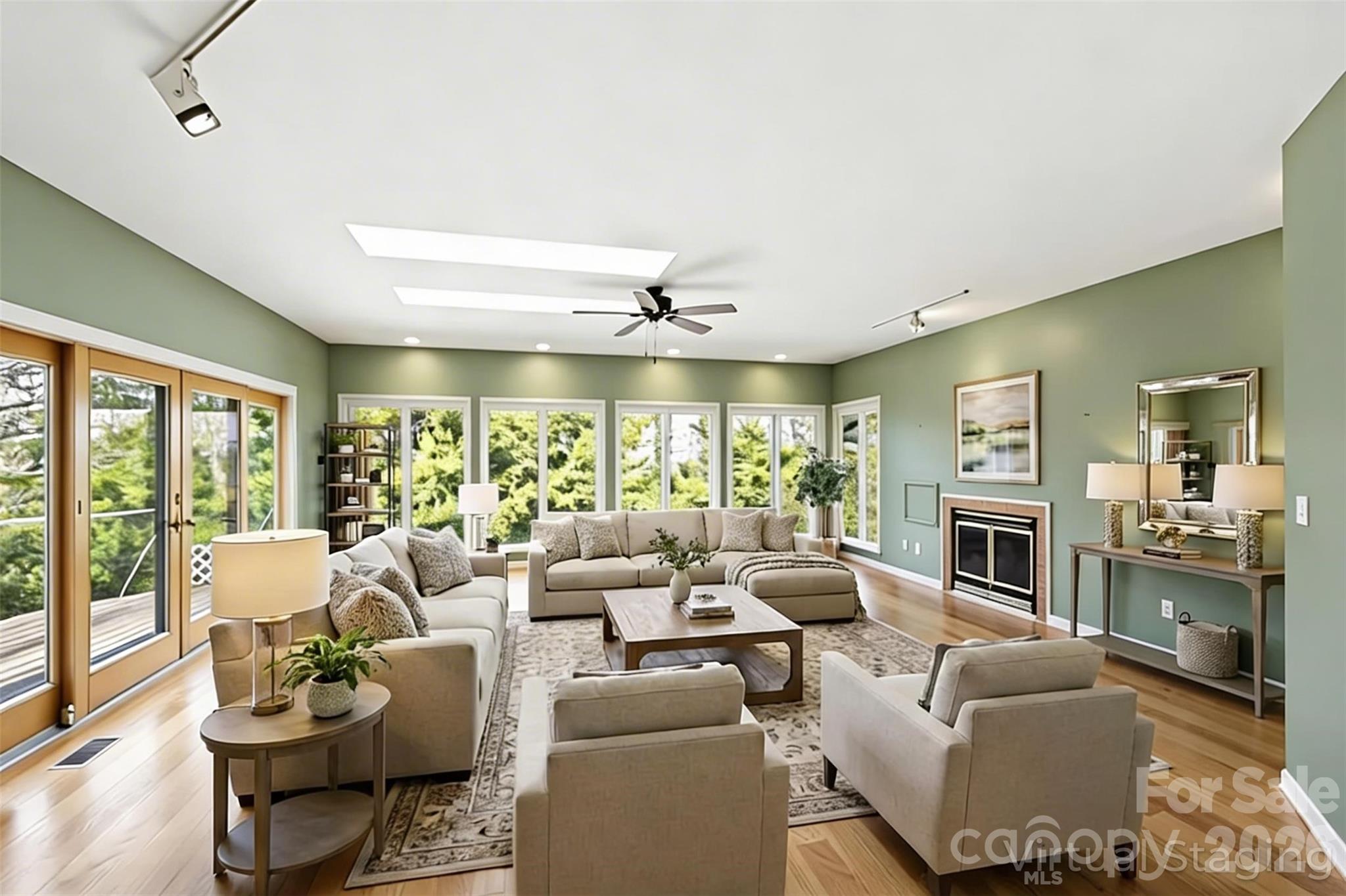 Staged living room with sage-green walls, a fireplace, and large windows overlooking trees.