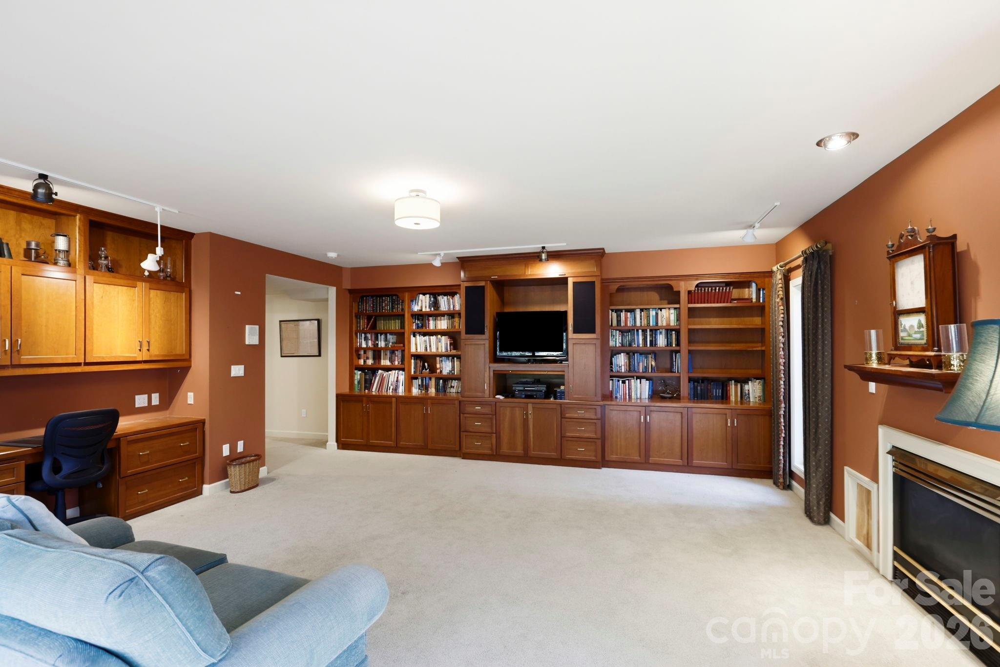 Furnished den with built-in wooden bookcases, a television, desk, and fireplace.