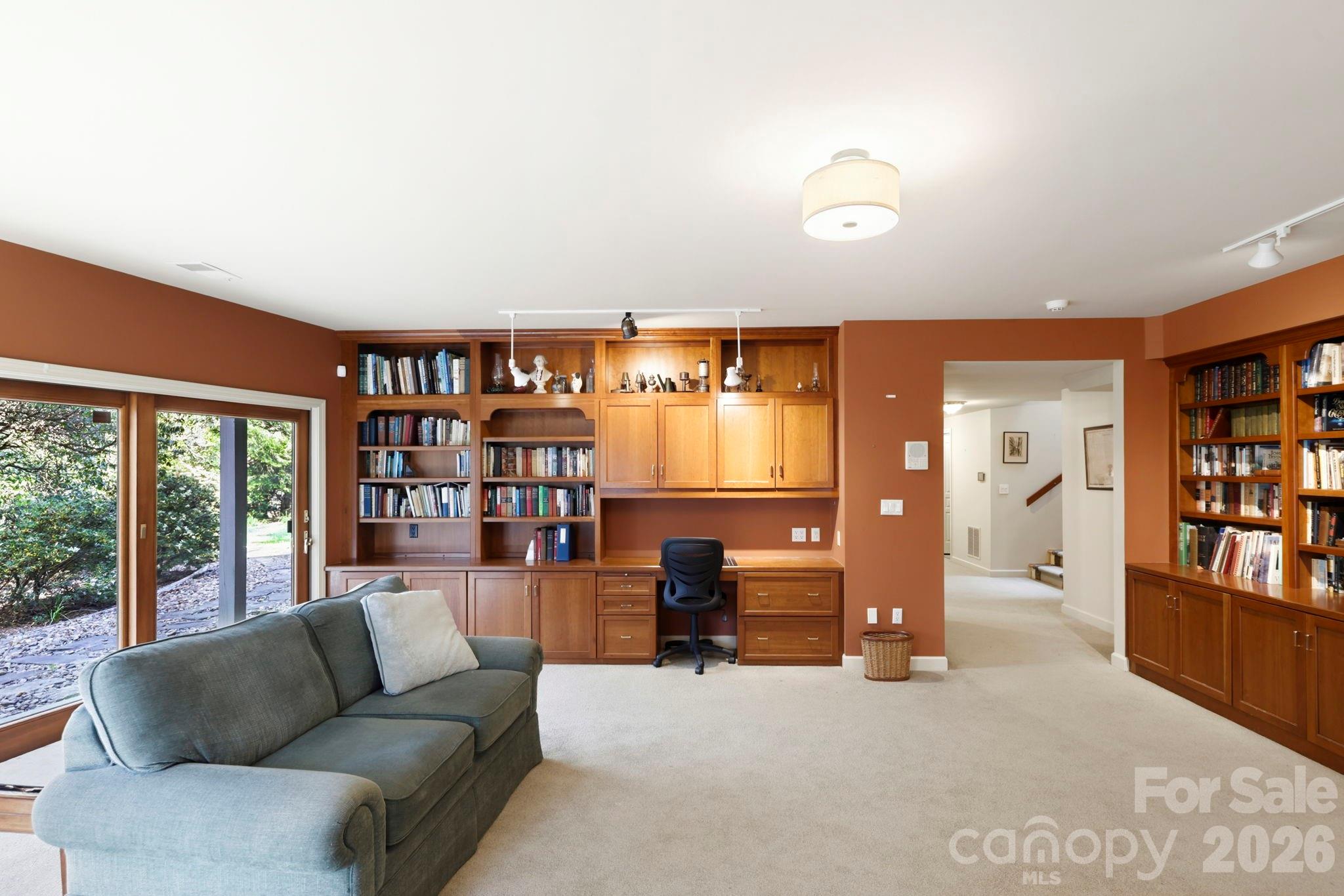 Home office with wood built-ins and bookshelves, desk, gray sectional, and sliding glass doors.