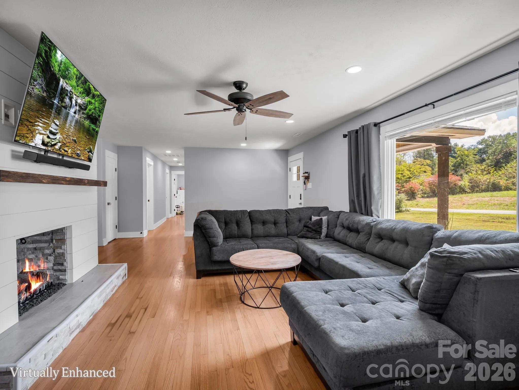 Furnished living room with a gray sectional, lit stone fireplace, and wide opening to a covered patio.