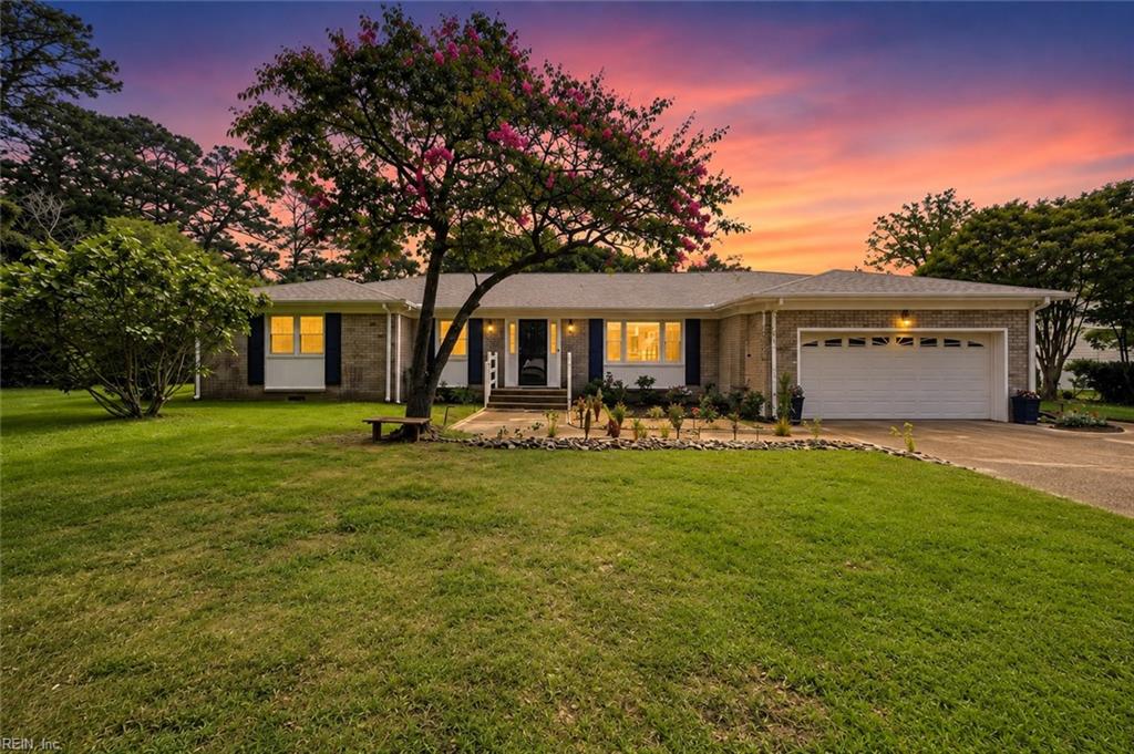 Brick ranch house with a two-car garage and flowering tree beneath a vivid sunset.