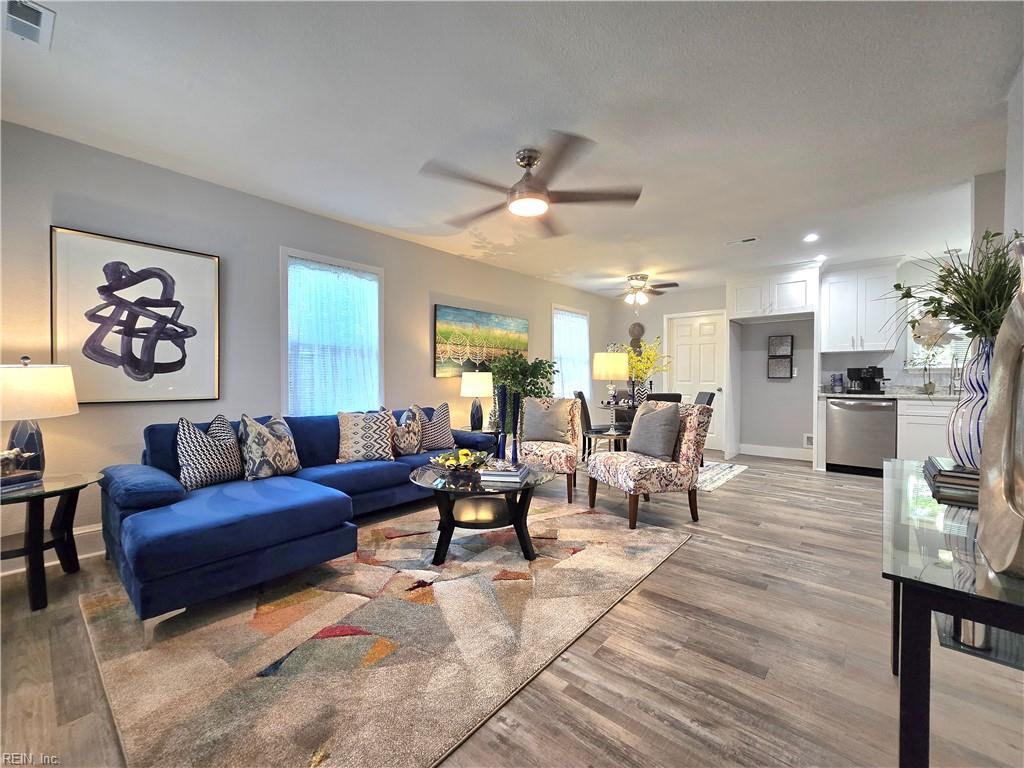 Open-plan living room with a blue sectional, patterned rug, dining area, and white kitchen.