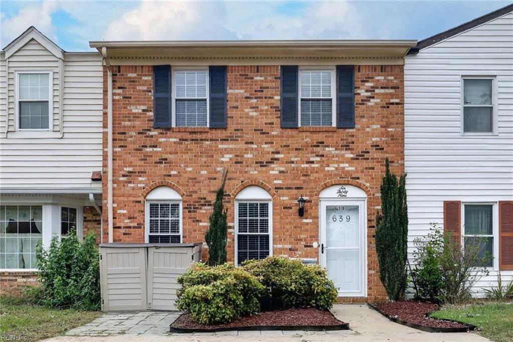 Brick townhouse with navy shutters, white entry door marked 639, and shrubs beside the walkway.
