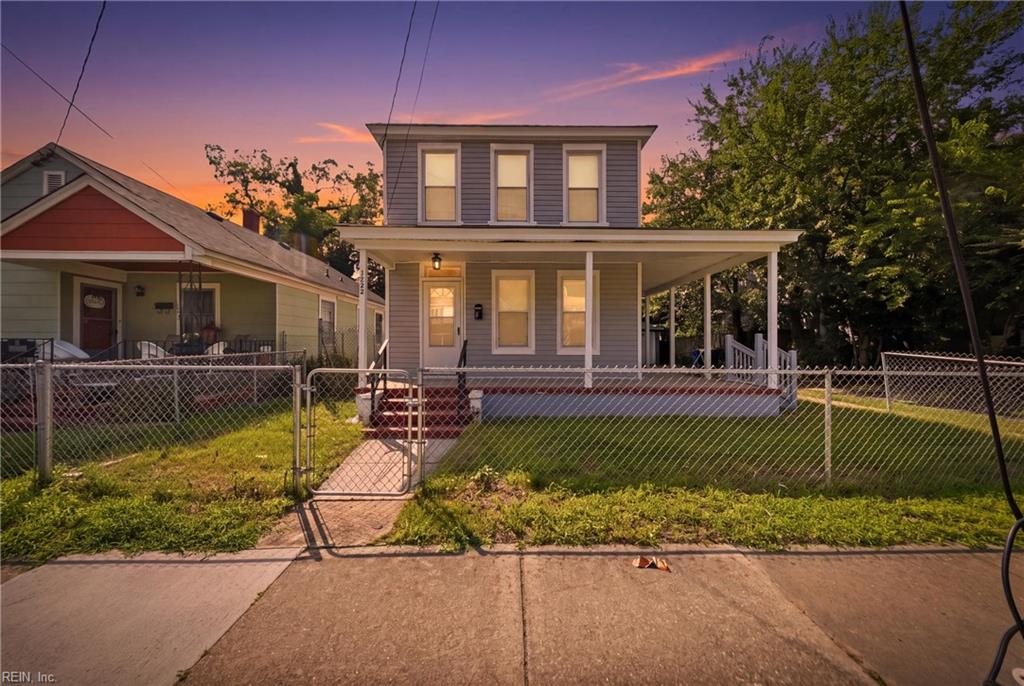 Two-story gray house with a covered porch and fenced front yard at dusk.
