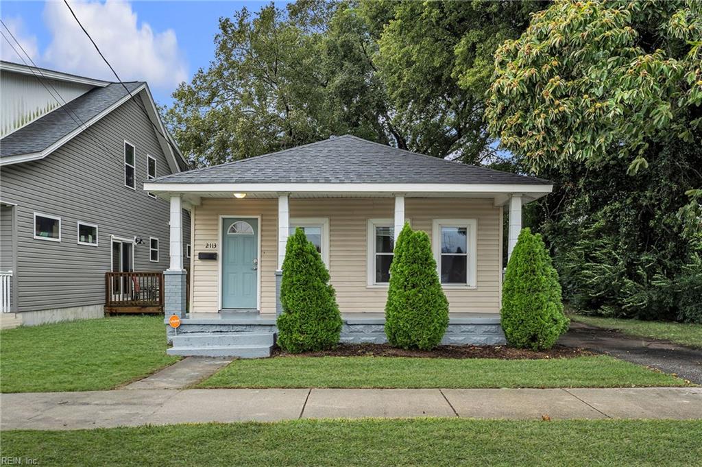 Single-story beige house with a turquoise front door, covered porch, and evergreen shrubs.